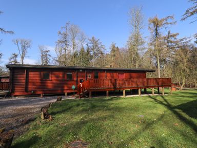 A red wooden cabin with a wooden deck and stairs surrounded by grass and trees at Great Leap in Louth