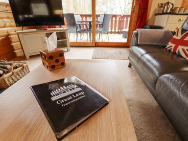 A living room with a wooden coffee table holding a guest information book and tissue box near a leather sofa and TV at Great Leap in Louth