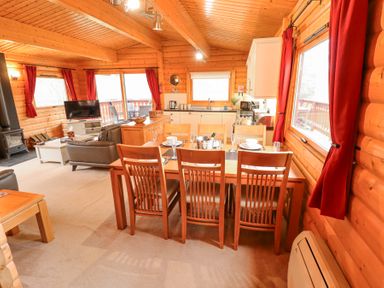 A wooden dining table with six chairs set with dishes in an open plan wooden cabin with red curtains and kitchen area at Great Leap in Louth