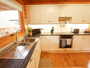 A kitchen with white cabinets a black countertop a stainless steel sink with a dish rack a microwave a knife block a toaster oven and wooden floors at Great Leap in Louth
