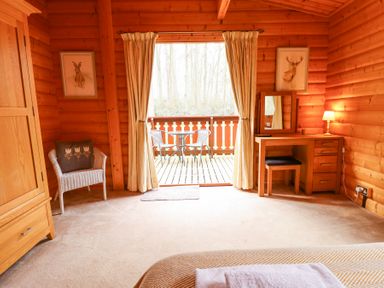 A wooden room with a wicker chair a wardrobe a dressing table with a mirror and lamp and a balcony with two chairs and a table at Great Leap in Louth