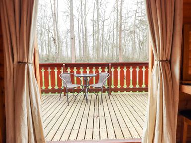 A wooden deck with a round table and two chairs viewed through open curtains at Great Leap in Louth