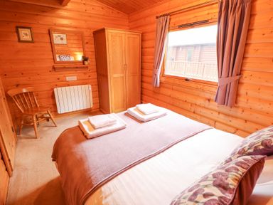 A wooden bedroom with a bed with folded towels a wardrobe a chair window with curtains and a mirror at Great Leap in Louth