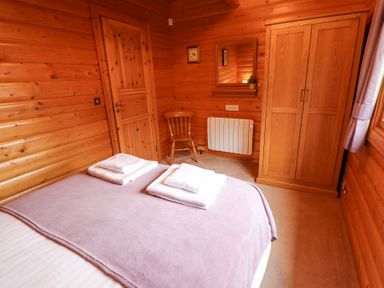 A bedroom with wooden walls a bed with folded towels a wooden chair a wall mirror and a wooden wardrobe at Great Leap in Louth