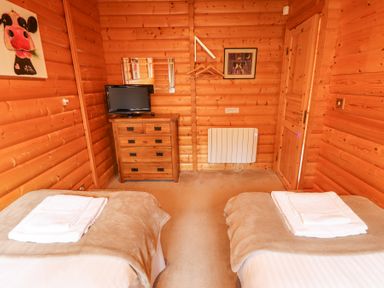 A wooden room with two single beds with towels on them a chest of drawers with a television on top and a door at Great Leap in Louth