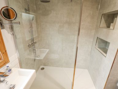 A bathroom with a shower area a glass shower screen a wall-mounted showerhead a hand shower a built-in shelf and a sink with a soap dispenser at Great Leap in Louth