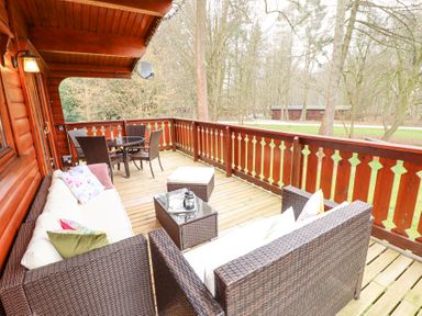 An outdoor wooden deck with wicker sofas cushions a glass table and chairs surrounded by trees at Great Leap in Louth