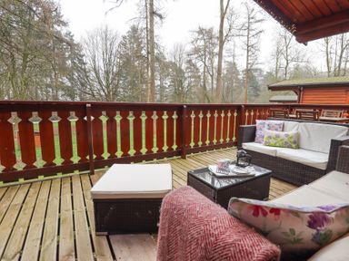 An outdoor wooden deck with cushioned wicker seating a small coffee table and a red wooden railing overlooking trees at Great Leap in Louth