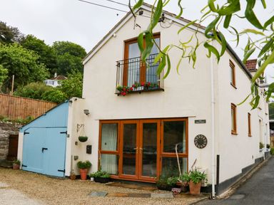 A two-story house with blue garage doors and wooden framed windows with plants outside at The Coach House The Grove in Combe Martin