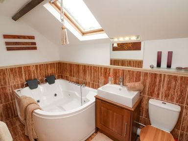 A bathroom with a corner bathtub a sink with cabinet a toilet and a skylight at The Coach House The Grove Combe Martin