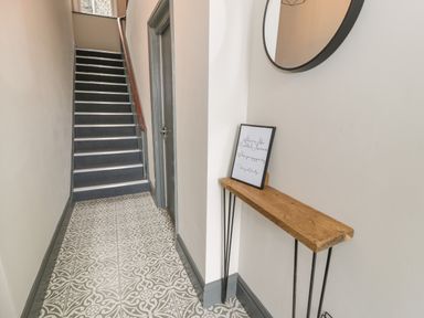 A hallway with patterned floor tiles a small wooden table with a framed picture and a round mirror on the wall at Emerald Suite in Barmouth