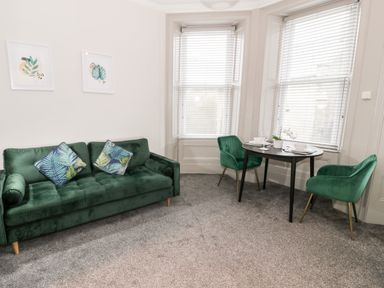 A living room with a green sofa two green chairs a black table and two framed pictures on the wall at Emerald Suite in Barmouth