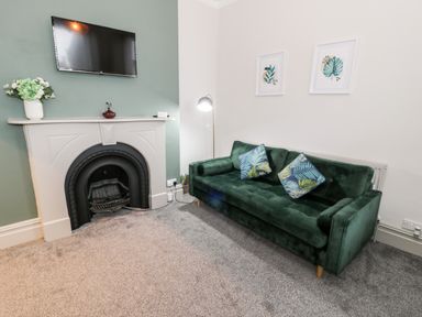 A living room with a green sofa and cushions near a fireplace with a TV mounted above it at Emerald Suite in Barmouth