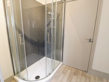 A shower with glass doors and a white tray next to a closed white door in a bathroom at Emerald Suite in Barmouth
