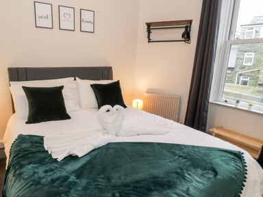 A bedroom with a made bed with green pillows and blanket and towel swans on top at Emerald Suite in Barmouth