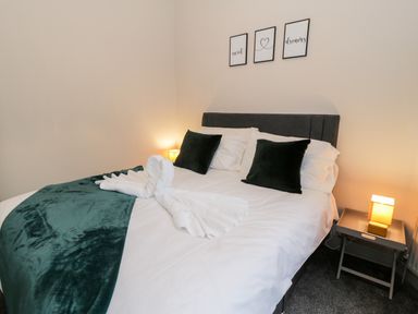 A bedroom with a bed with white sheets and green pillows and blankets and two lamps on bedside tables at Emerald Suite in Barmouth