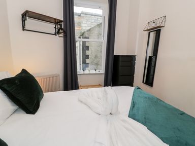 A bedroom with a bed with pillows and a towel swan next to a window with curtains and a black dresser and a mirror on the wall at Emerald Suite in Barmouth