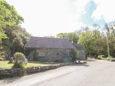 A stone cottage with green window frames surrounded by trees and a stone wall at Glyn Yr Efail in Moylegrove nr Newport and Cardigan