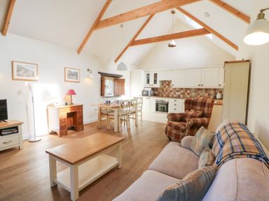An open plan living room and kitchen with wooden beams a dining table and chairs a sofa and an armchair at Glyn Yr Efail in Moylegrove nr Newport and Cardigan