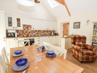 A kitchen with a dining table set with blue dishes and glasses and a plaid armchair at Glyn Yr Efail in Moylegrove nr Newport and Cardigan