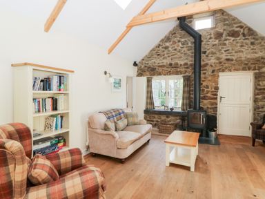A living room with a stone wall and wood burning stove a sofa armchairs a bookcase and a wooden coffee table at Glyn Yr Efail in Moylegrove nr Newport and Cardigan
