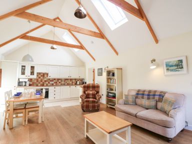 A kitchen and living area with wooden beams a dining table an armchair a sofa and a bookcase at Glyn Yr Efail in Moylegrove nr Newport and Cardigan