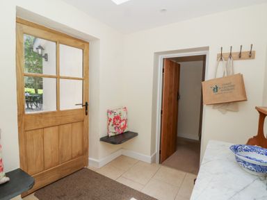 A hallway with a wooden door, wall hooks with bags, small shelves with cushions, and a marble countertop with a blue and white bowl at Glyn Yr Efail in Moylegrove nr Newport and Cardigan