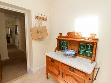 A hallway with a wooden cabinet with a marble top and decorative tiles and a bag hanging on wall hooks at Glyn Yr Efail in Moylegrove nr Newport and Cardigan