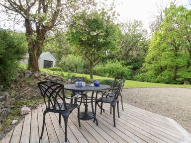 An outdoor patio area with a round metal table and four chairs surrounded by trees and grass at Glyn Yr Efail in Moylegrove nr Newport and Cardigan