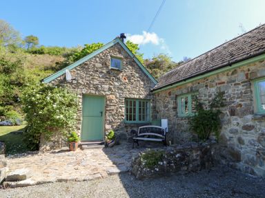 A stone cottage with green window frames and door with a bench outside and plants at Glyn Yr Efail in Moylegrove nr Newport and Cardigan