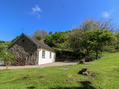A small stone and white cottage with green trim beside grassy area and trees at Glyn Yr Efail Moylegrove nr Newport and Cardigan