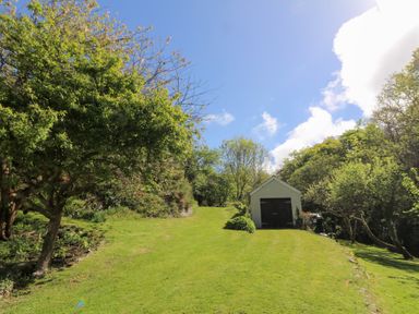 A green lawn sloping upwards with trees on both sides and a small white shed at the top at Glyn Yr Efail in Moylegrove nr Newport and Cardigan