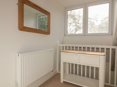 A corner of a room with a white radiator wooden framed mirror and a white cabinet with drawers at Stores & Supplies in Bodmin