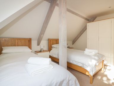 A bedroom with two single beds wooden headboards white bedding and towels a wooden beam a white wardrobe and two bedside tables at Stores & Supplies in Bodmin