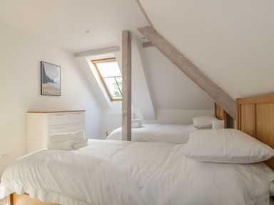 A bedroom with two single beds white bedding wooden headboards a dresser under a slanted ceiling with exposed beams and a skylight window at Stores & Supplies in Bodmin