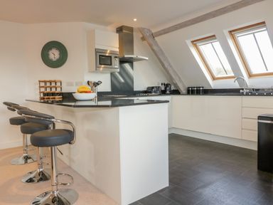 A kitchen with a black countertop island with stools a microwave oven and two skylight windows at Stores & Supplies in Bodmin
