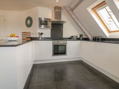 A kitchen with white cabinets a built-in oven microwave and black countertop at Stores & Supplies in Bodmin