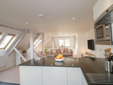An open plan kitchen and living area with a black countertop island a beige sofa and dining table with chairs at Stores & Supplies in Bodmin