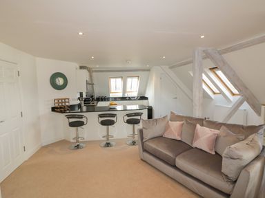 An open plan room with a kitchen counter with three bar stools and a sofa with cushions at Stores & Supplies in Bodmin