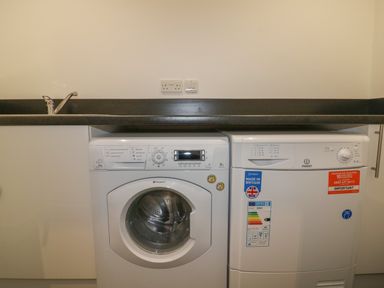 A laundry area with a washing machine and a dryer under a countertop with a sink at Stores & Supplies in Bodmin
