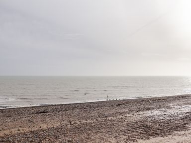 A pebble beach with wooden posts extending into a calm sea under a cloudy sky at Sparrows Den Lodge in Winchelsea Beach