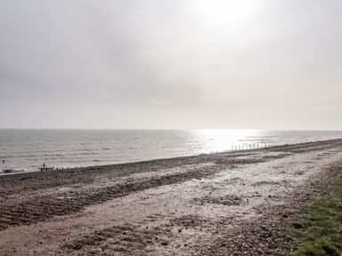 A pebbled beach with sea and sky in the background and a strip of grass on the side at Sparrows Den Lodge in Winchelsea Beach