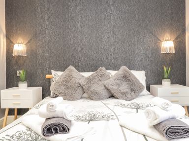 A bed with gray pillows and folded towels on white and gray bedding and white nightstands with plants at Sparrows Den Lodge in Winchelsea Beach
