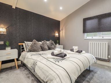 A bedroom with a bed made with patterned linens and towels on top with bedside tables and windows at Sparrows Den Lodge in Winchelsea Beach