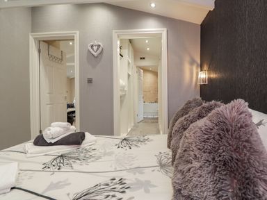 A bedroom with a bed holding folded towels and pillows and an open door leading to a bathroom at Sparrows Den Lodge Winchelsea Beach