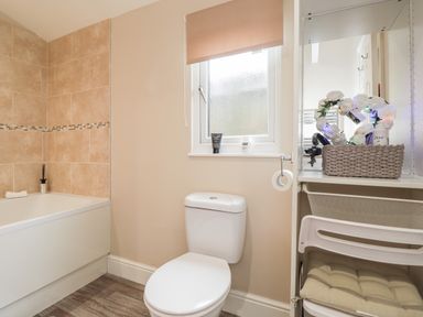 A bathroom with a bathtub, toilet, window, and a shelving unit with a basket and cushions at Sparrows Den Lodge Winchelsea Beach