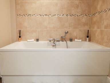 A bathtub with a faucet handheld shower and decorative items on the edge in a bathroom at Sparrows Den Lodge in Winchelsea Beach