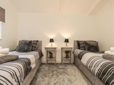 A bedroom with two single beds striped bedding nightstands and lamps at Sparrows Den Lodge Winchelsea Beach