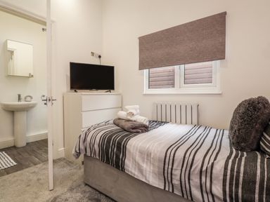 A bedroom with a single bed and TV on dresser next to an open door showing a sink at Sparrows Den Lodge in Winchelsea Beach