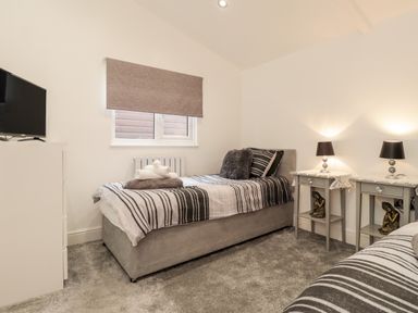 A bedroom with two single beds side tables with lamps and a television at Sparrows Den Lodge in Winchelsea Beach